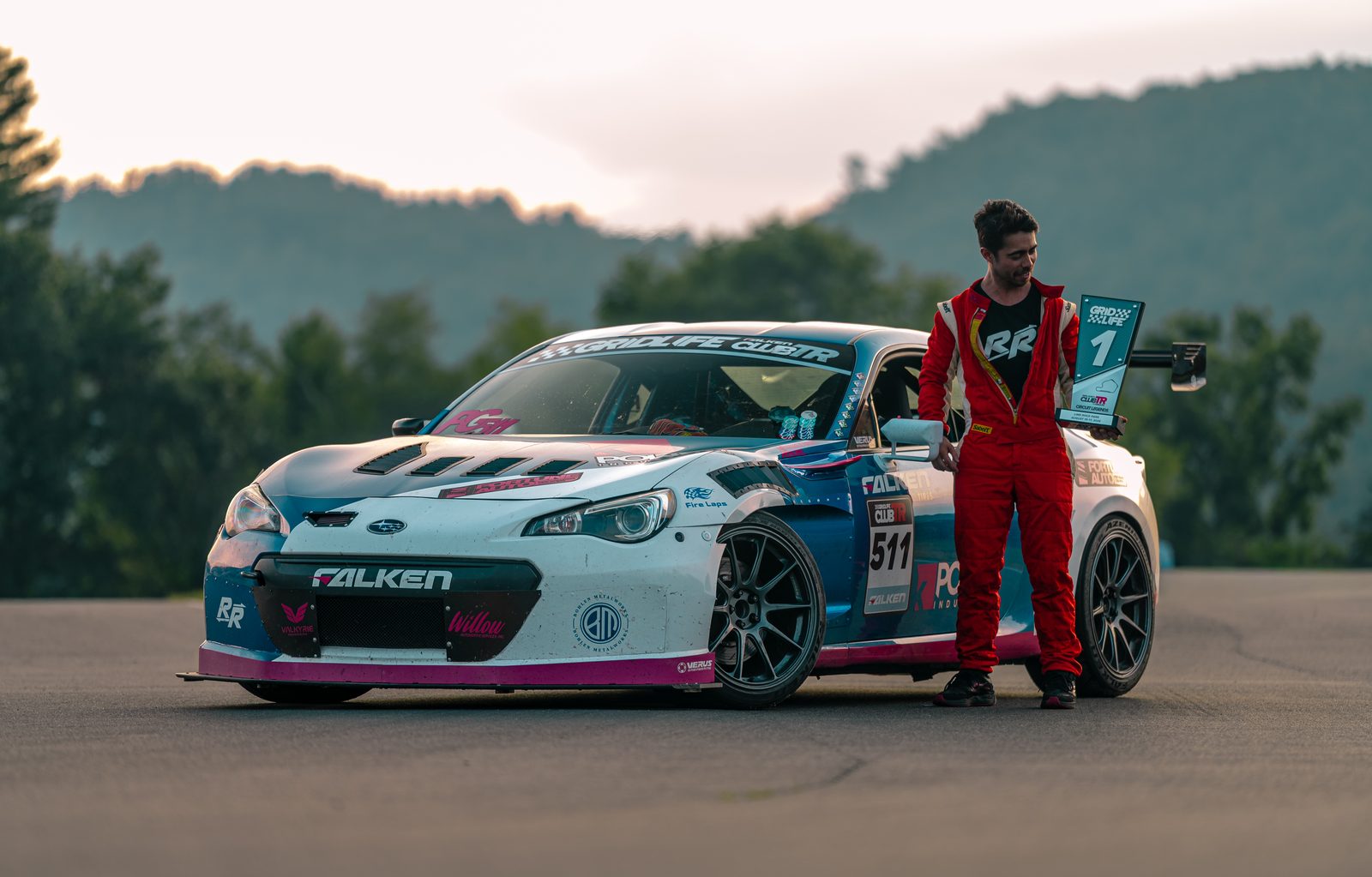 Peter Granberg in a red race suit beside the #511 K-swapped BRZ, holding a GRIDLIFE ClubTR first-place trophy at Lime Rock Park